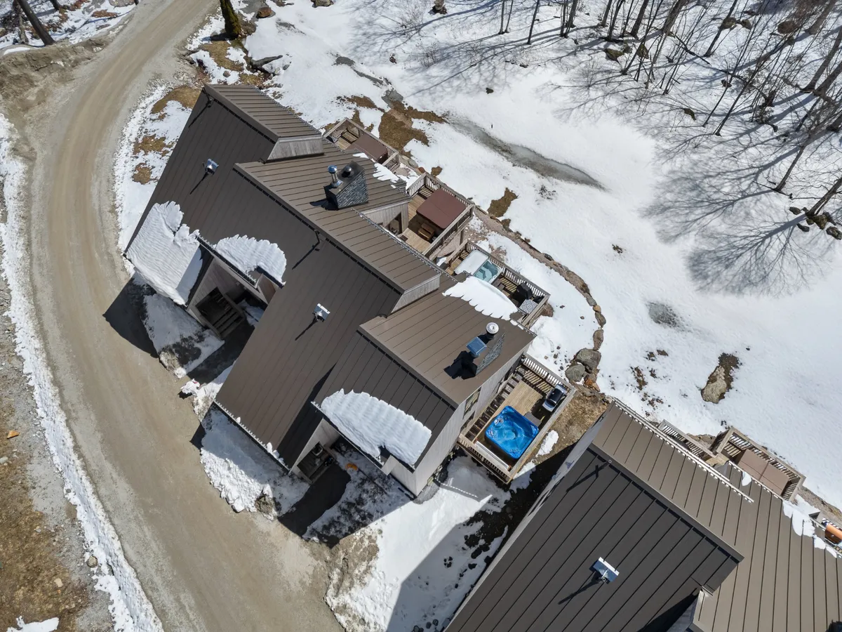 This exterior image captures the rooftops of the houses with a prominent hot tub in the foreground, set against a serene, snow-covered landscape. The setting conveys a sense of tranquil relaxation and highlights the outdoor amenities guests look forward to after a day of adventure.