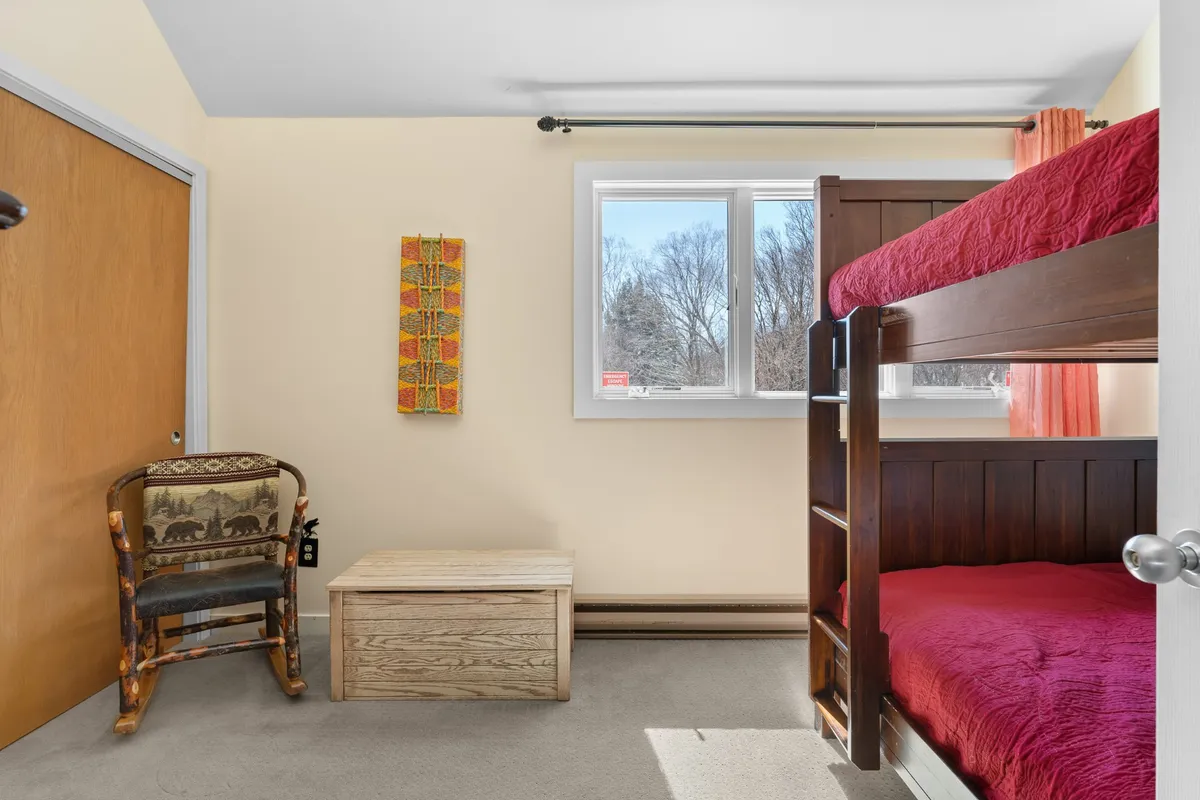 An inviting interior shot featuring a full-over-full bunk bed, a window with natural light, colorful wall art, a wooden chair, and a storage box. The space feels playful and versatile—ideal for children or groups, and highlights safe, flexible sleeping arrangements.