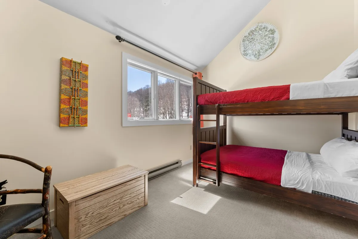 A vibrant bunk bedroom with full-over-full bunk beds, colorful wall art, and large windows that provide plenty of daylight. The room radiates a playful and comfortable energy, perfect for kids or groups.