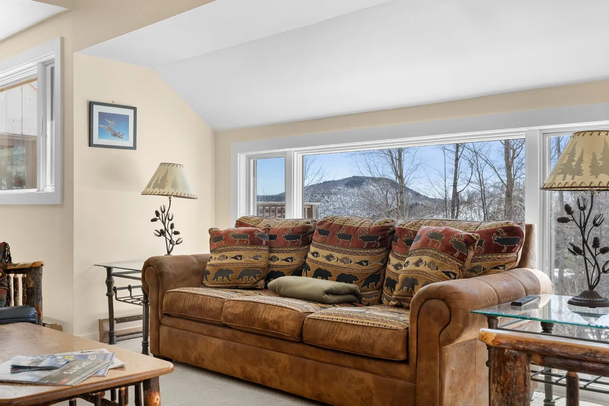 A tastefully appointed living area with a leather sofa and decorative pillows, large windows framing a sweeping mountain view, and table lamps that enhance the inviting ambiance. The space is filled with natural light, highlighting both comfort and the beautiful surroundings.