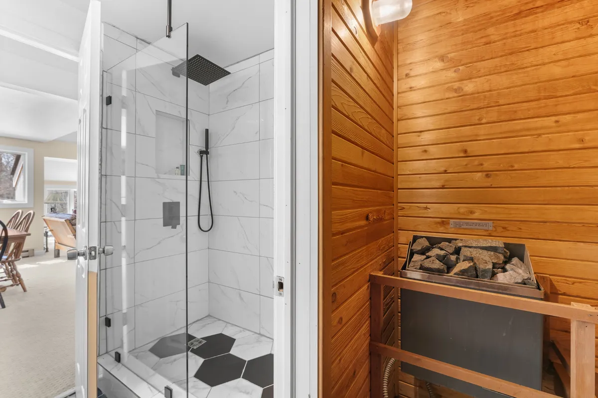 A combined view of a glass shower enclosure and a wooden sauna interior, framed by a tranquil, modern setting. The inviting warmth of the sauna is complemented by the sleek, refreshing look of the shower area.