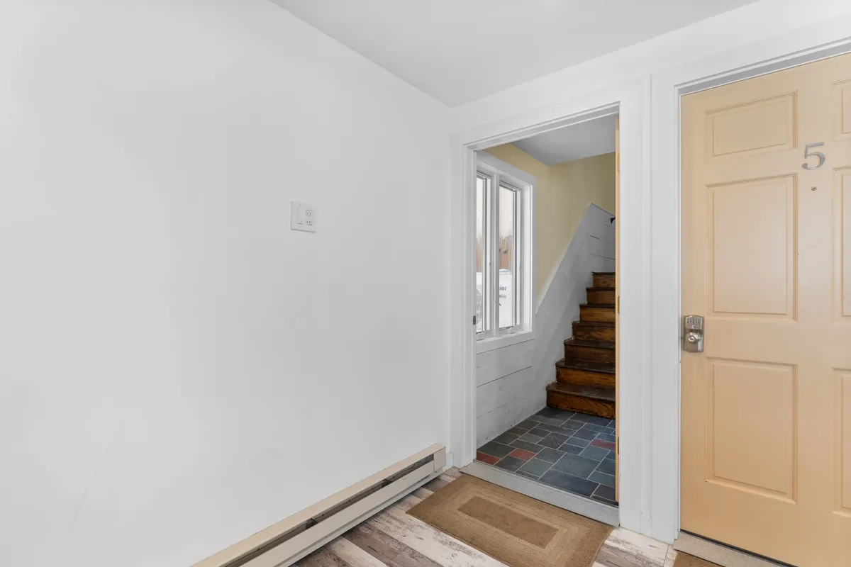 The image features the home's front door, an inviting staircase, and ample windows that let in natural light. The scene evokes the experience of arrival and departure, highlighting the welcoming atmosphere and easy movement between indoor and outdoor spaces.