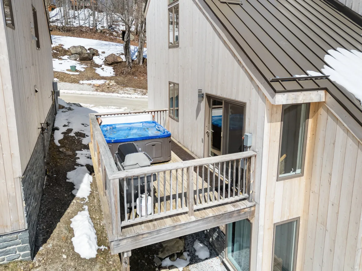 A private outdoor hot tub sits on a wooden deck overlooking a snowy landscape, framed by trees and the gentle morning light. The inviting water steams against the cold winter air, creating a perfect après-ski retreat.