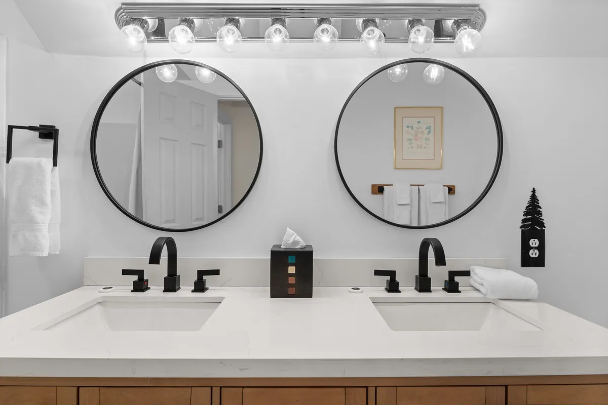 A modern bathroom with double sinks, stylish circular mirrors, and a contemporary light fixture. The clean lines and fresh ambiance set the tone for a spa-inspired self-care routine.